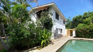 A house with a swimming pool, surrounded by lush greenery and a clear blue sky. - Tzalahua House (Manzanillo)