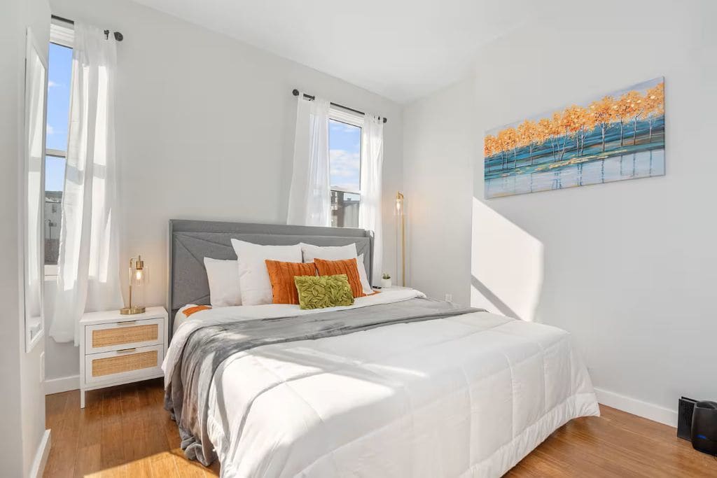 Quarto com cama, mesas de cabeceira, um quadro e uma janela com cortinas.