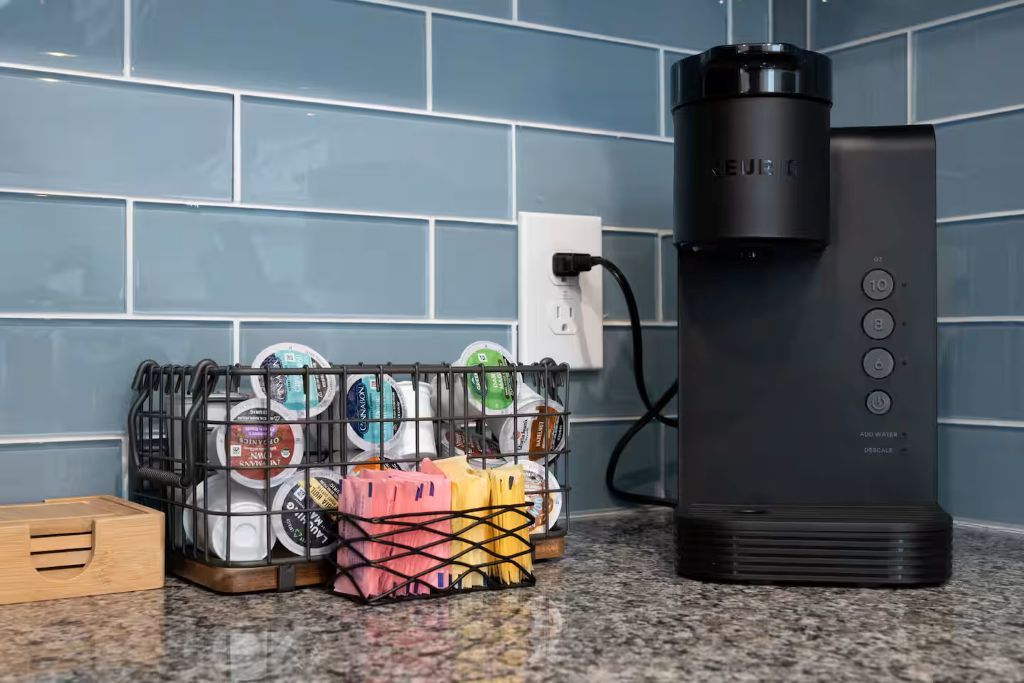 Een keuken met een koffiezetapparaat, een stopcontact en een mand vol afwas.