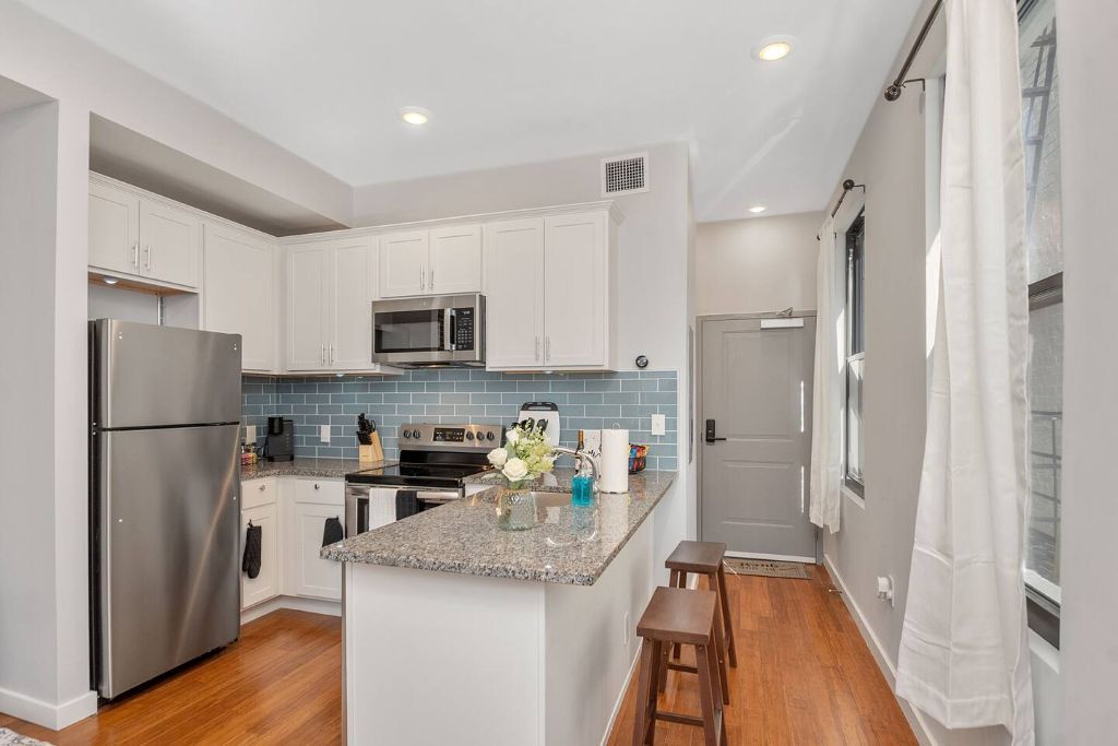 A modern kitchen with white cabinets, a stainless steel refrigerator, a microwave, and a granite countertop.