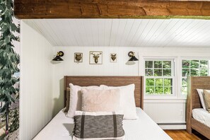 A bedroom with a wooden headboard, a bed with white bedding, a window with a view of greenery, and wall-mounted wall art. - Cozy Quechee Hollow Condo with Pond Views & Club Access (Hartford)