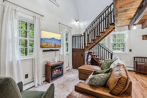 Ein Wohnzimmer mit Kamin, Fernseher, Treppe und Sofa.
