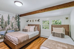 Ein Schlafzimmer mit zwei Betten, einer Wandmalerei von Bäumen und Bergen sowie einem Fenster mit Blick auf Grünfläche.