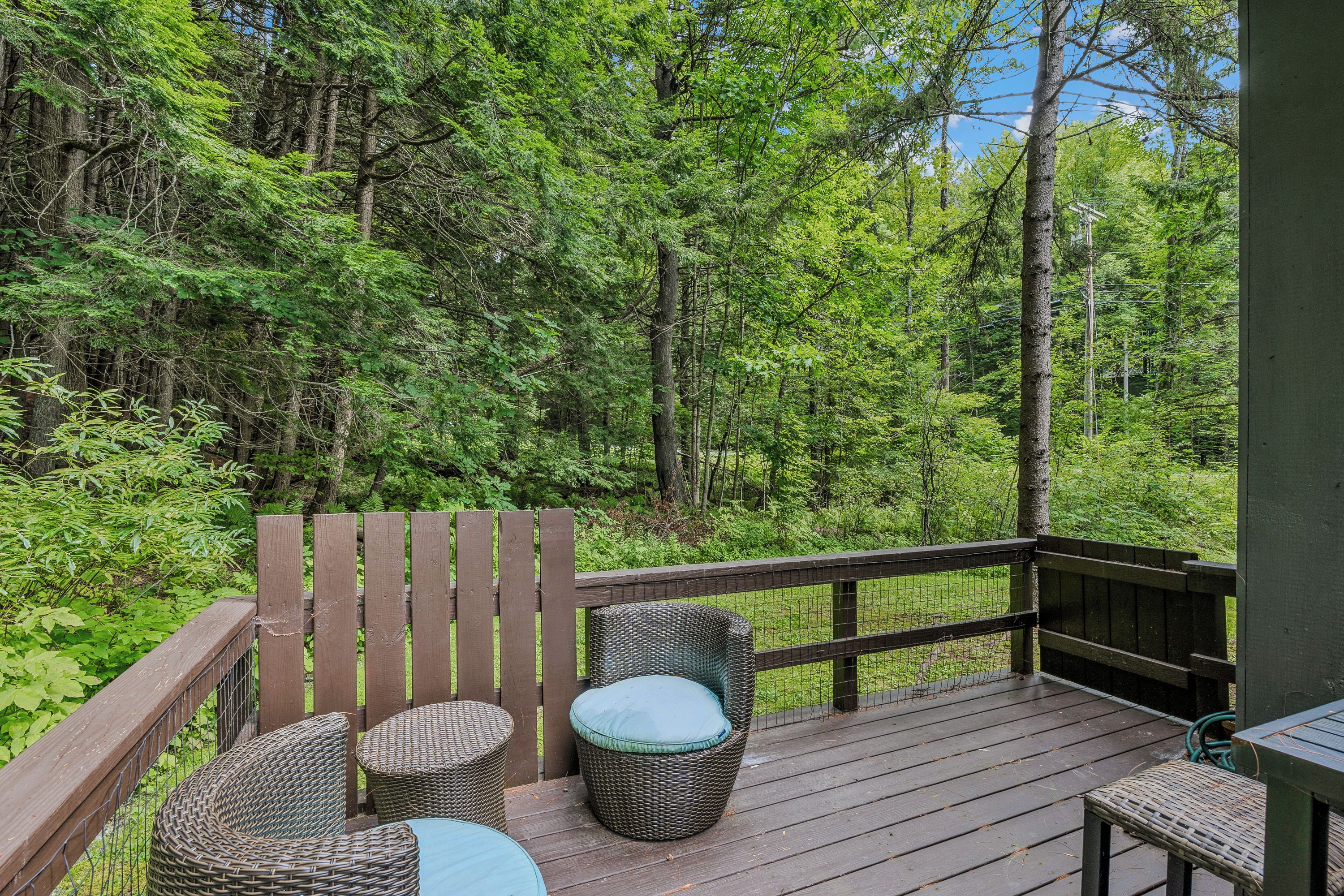 Une terrasse en bois, meublée de mobilier en osier, avec vue sur une forêt dense.