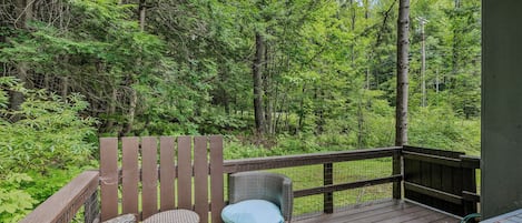 Une terrasse en bois, meublée de mobilier en osier, avec vue sur une forêt dense.