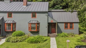 A two-story building with a grey exterior, red-framed windows, and a chimney. - Cozy Quechee Hollow Condo with Pond Views & Club Access (Hartford)