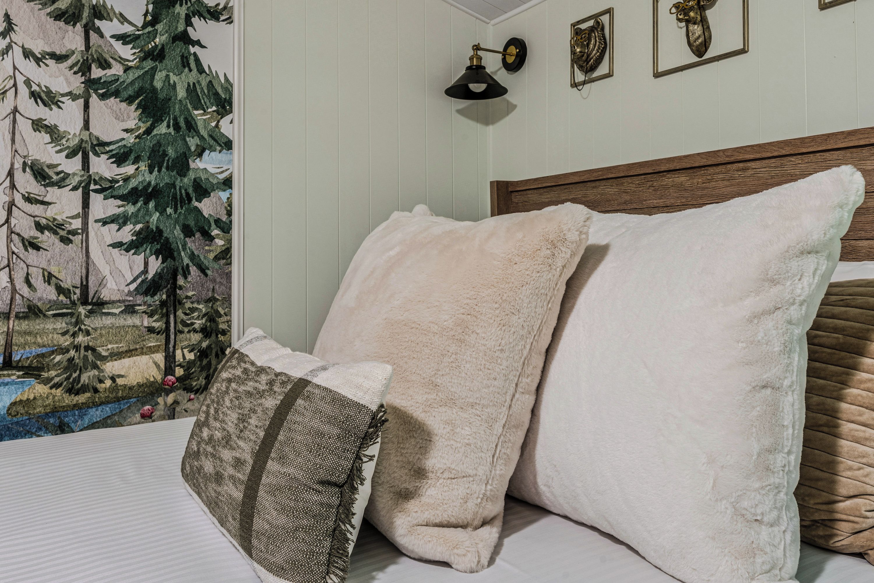 Una cama con múltiples almohadas y cabecero, una lámpara de pared y un cuadro enmarcado.