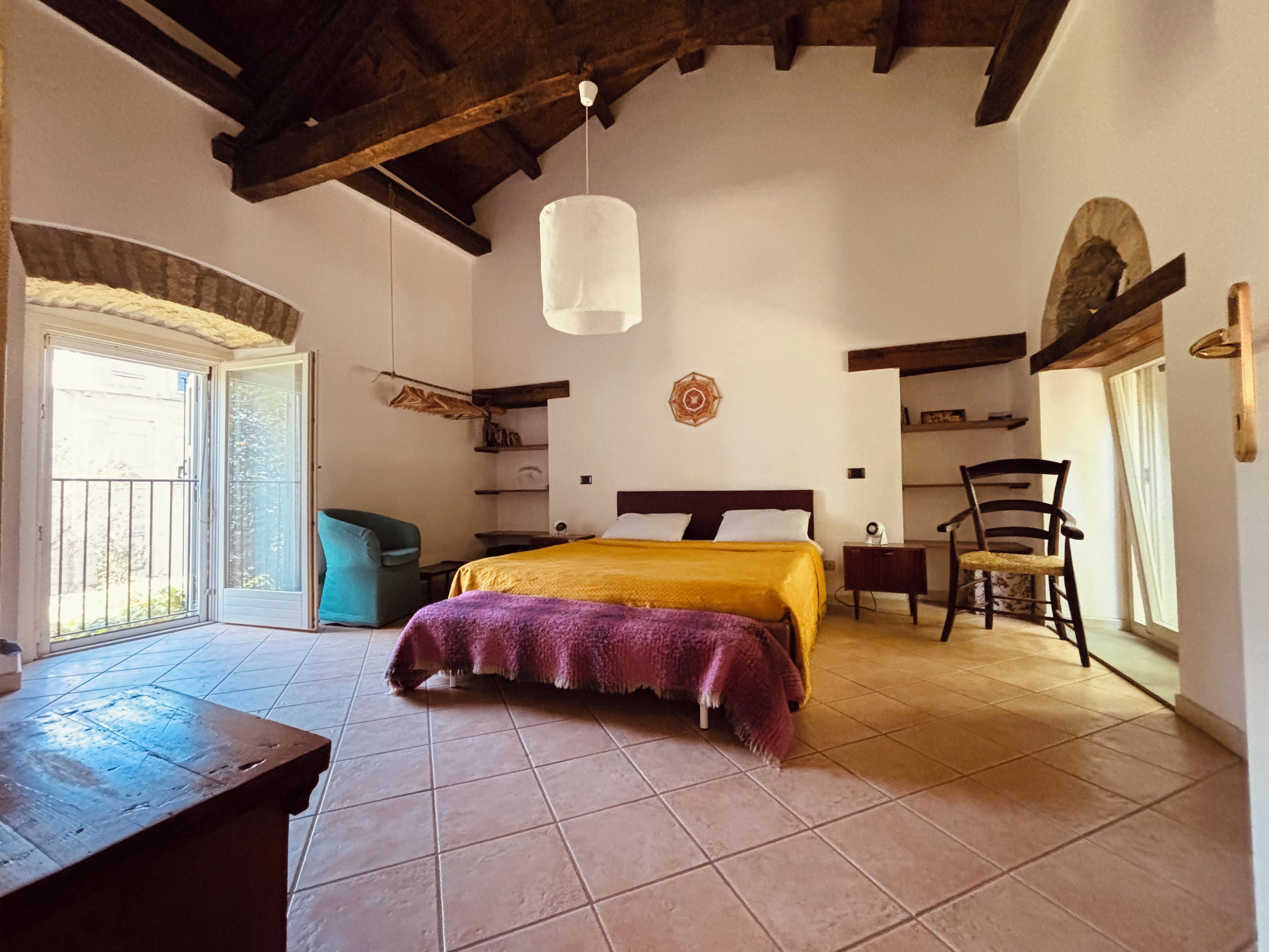 A bedroom with a bed, a chair, a table, and a hanging light fixture.