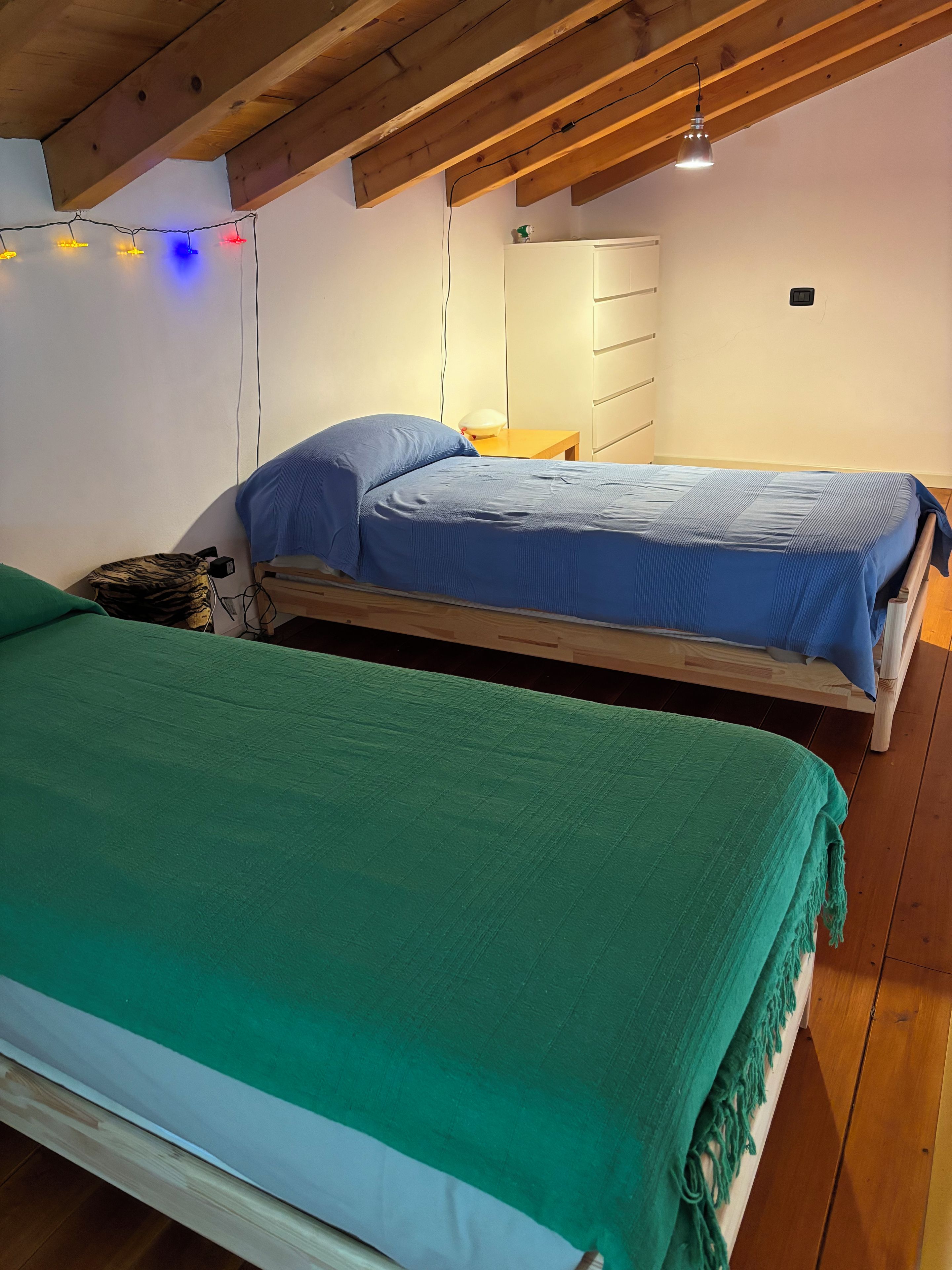 A room with two beds, wooden flooring, a white wardrobe, and a ceiling with exposed beams.