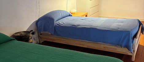 Una habitación con dos camas, suelo de madera, un armario blanco y un techo con vigas a la vista.
