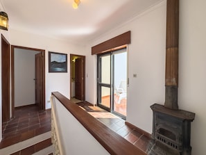 Ein Flur mit einer Holztreppe, einem Kamin und einer Tür, die auf einen Balkon mit Gartenmöbeln führt.
