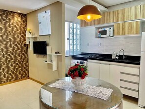 A modern kitchen with a built-in microwave, a flat-screen TV, and a dining area with a glass table. - Apartment 201 · Practical flat close to everything (Belém)
