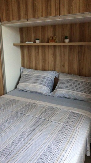 A bed with patterned bedding, a wooden headboard, and a shelf with decorative items. - Apartment 201 · Practical flat close to everything (Belém)
