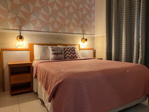 Een slaapkamer met een bed, twee nachtkastjes, een hoofdeinde en een plafond met een geometrisch patroon.