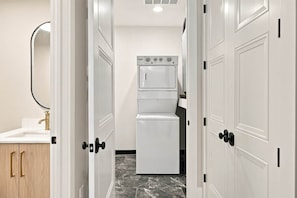 Un baño de hotel con un lavamanos blanco, un espejo y una lavadora blanca.