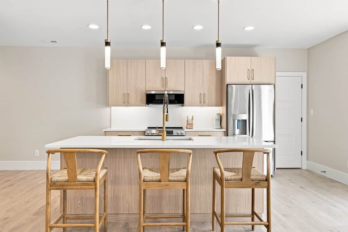 Una cocina moderna con una isla central, sillas de madera, iluminación colgante y electrodomésticos de acero inoxidable.