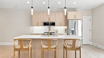 Una cocina moderna con una isla central, sillas de madera, iluminación colgante y electrodomésticos de acero inoxidable.