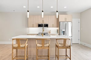 Una cocina moderna con una isla central, sillas de madera, iluminación colgante y electrodomésticos de acero inoxidable.