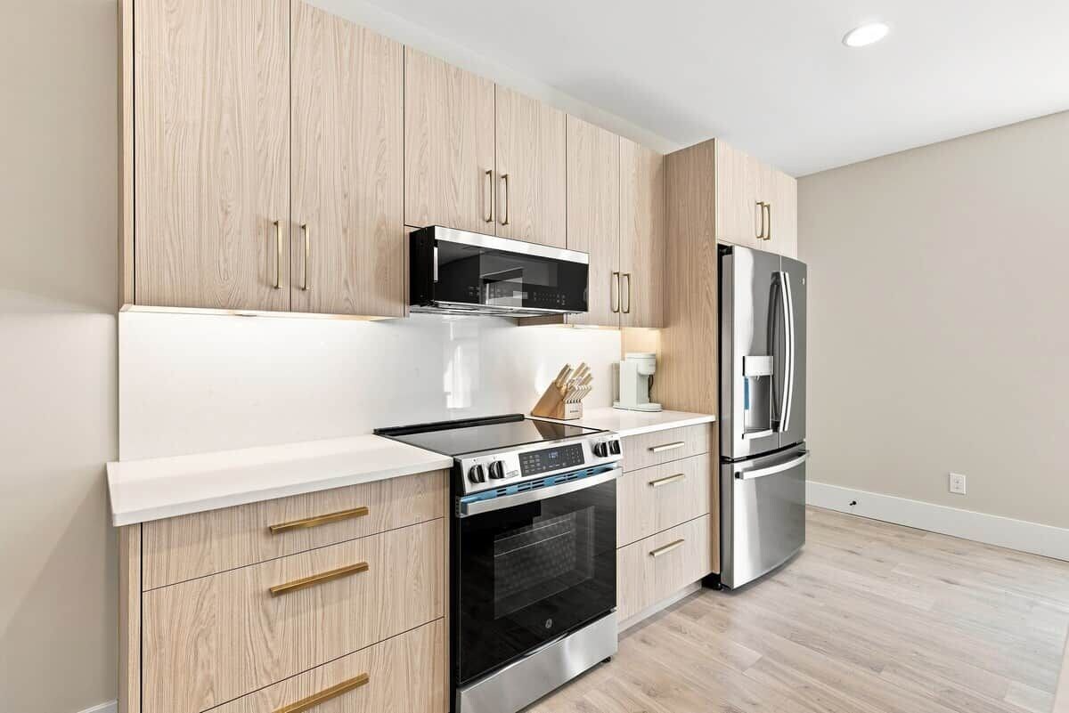 A modern kitchen with wooden cabinets, a stainless steel refrigerator, a microwave, and a built-in oven.
