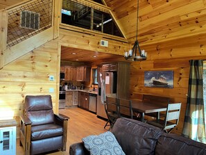 A cabin interior with a dining area, kitchen, and a loft bedroom with a window. - Cozy Bear 2 located on Turkey Nest Road (Gatlinburg)