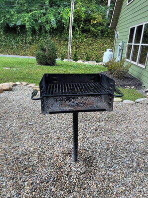 En grill på ett grusunderlag, med ett hus och grönska i bakgrunden.