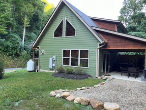 A green house with a sloped roof, a covered patio, and a gravel driveway with rocks. - Cozy Bear 2 located on Turkey Nest Road (Gatlinburg)