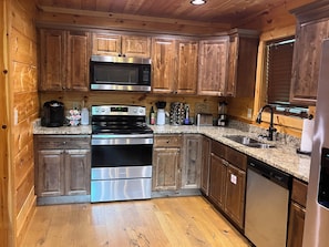 A kitchen with wooden cabinets, stainless steel appliances, granite countertops, and a dishwasher. - Cozy Bear 2 located on Turkey Nest Road (Gatlinburg)