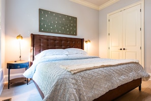 Une chambre à coucher avec un grand lit, deux lampes de chevet, une œuvre d’art accrochée au mur et une porte fermée.
