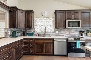 A modern kitchen with dark wood cabinets, a stainless steel dishwasher, a built-in oven, and a microwave. - New Listing - Dog-Friendly Pool Home in Peoria 15 mins from State Farm Stadium! (Peoria)