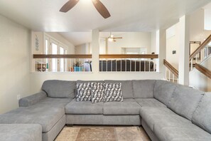 A modern living room with a grey sectional sofa, patterned throw pillows, a ceiling fan, and a view of a staircase. - New Listing - Dog-Friendly Pool Home in Peoria 15 mins from State Farm Stadium! (Peoria)