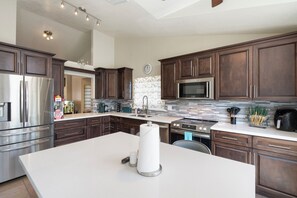 Een moderne keuken met donkerhouten kastjes, roestvrijstalen apparatuur, een groot eiland en een betegelde spatwand.
