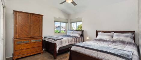 A bedroom with two beds, a wooden dresser, and a ceiling fan.