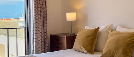 A hotel room with a bed, a nightstand, a lamp, and a view of the cityscape.