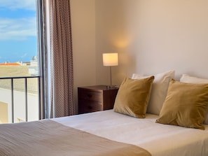 A hotel room with a bed, a nightstand, a lamp, and a view of the cityscape. - Alto da Villa by Acasadascasas (Mafra)