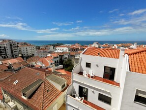 A coastal cityscape with terracotta-tiled buildings, balconies, and a view of the sea. - Alto da Villa by Acasadascasas (Mafra)