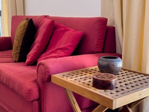 Un canapé rouge avec des coussins, une petite table en bois ornée d’un vase décoratif et un coussin à motifs.
