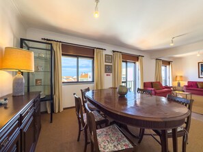 A hotel room with a dining table, chairs, a sofa, and a view of the cityscape. - Alto da Villa by Acasadascasas (Mafra)