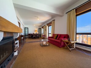 A spacious living room with a fireplace, a red sofa, a dining area, and large windows offering a view. - Alto da Villa by Acasadascasas (Mafra)
