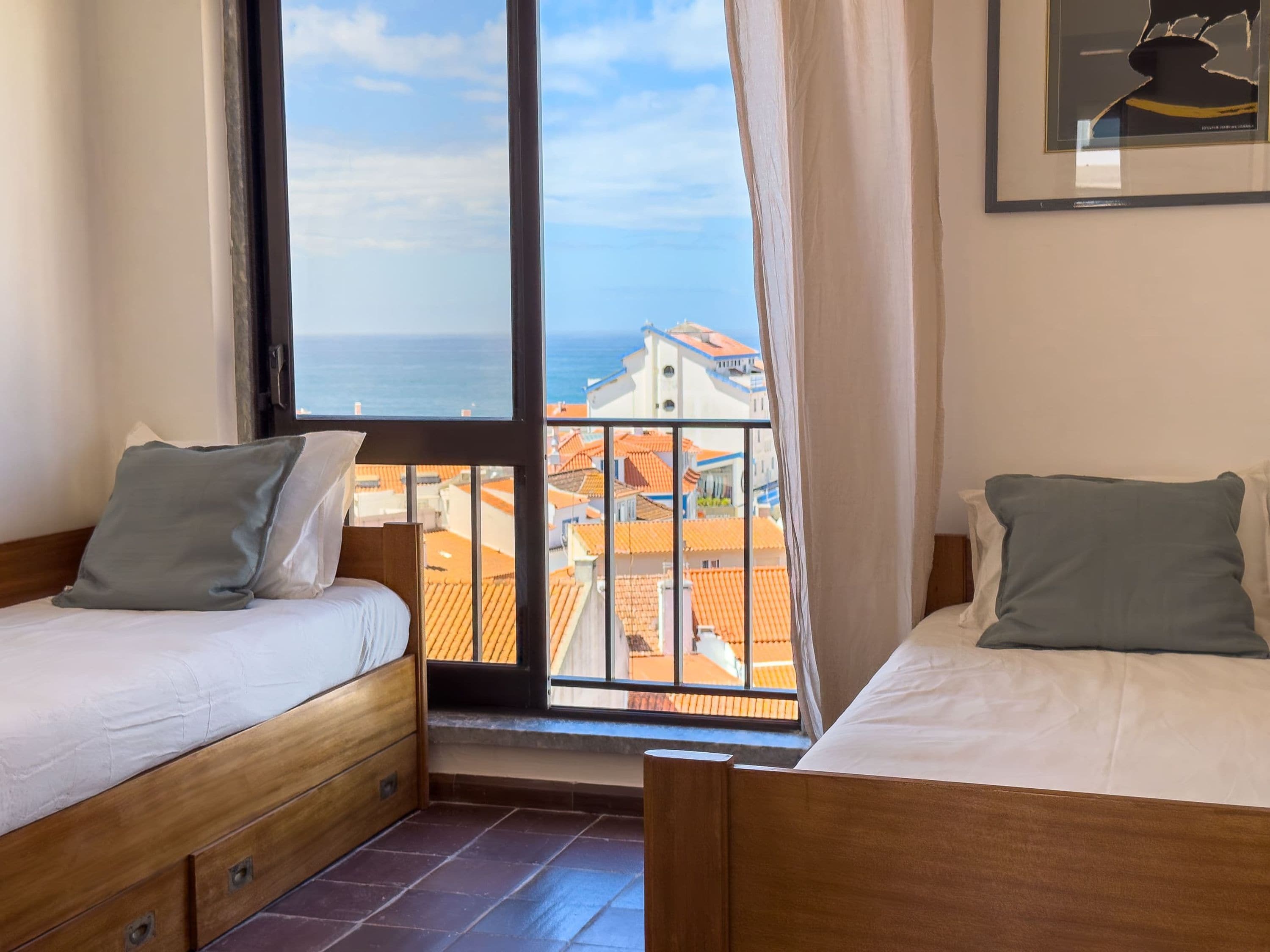 Ein Zimmer mit zwei Betten, einem großen Fenster und Blick auf Gebäude und das Meer.