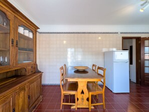 A kitchen with a wooden table, chairs, a cabinet with glass doors, and a white refrigerator. - Alto da Villa by Acasadascasas (Mafra)