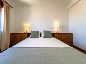 Une chambre d’hôtel avec un grand lit, deux tables de chevet avec des lampes et une fenêtre avec des rideaux.