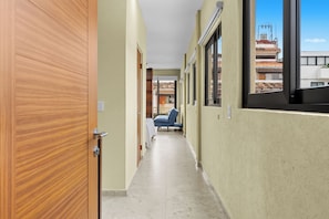 Un passadís amb una porta de fusta, un llit amb mantell blau i una finestra que donava a edificis.