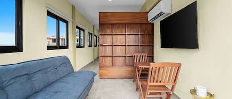 Une pièce avec un canapé bleu, une bibliothèque en bois, une table avec des chaises et un téléviseur fixé au mur.