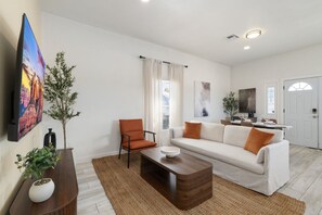Uma sala de estar moderna com sofá, poltrona, mesa de centro e televisão de tela plana na parede.