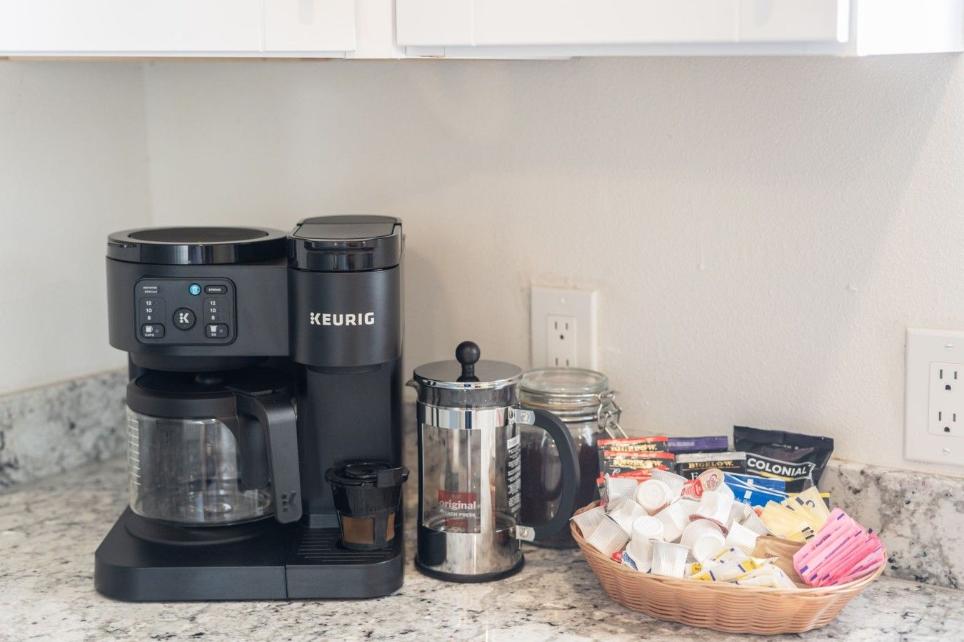 A coffee maker, a French press, and a basket of coffee pods on a kitchen counter.