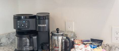 A coffee maker, a French press, and a basket of coffee pods on a kitchen counter.