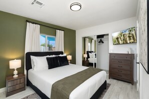 Quarto com cama, mesas de cabeceira, cômoda, espelho e televisão.