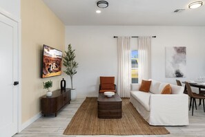 A modern living room with a sofa, a coffee table, a TV, and a dining area with chairs and a table. - Phoenix Furnished with 2 Queen Beds & EV Charger! (Phoenix)