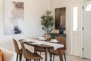 A dining area with a table set for four, chairs, a vase with greenery, and abstract art on the walls. - Phoenix Furnished with 2 Queen Beds & EV Charger! (Phoenix)