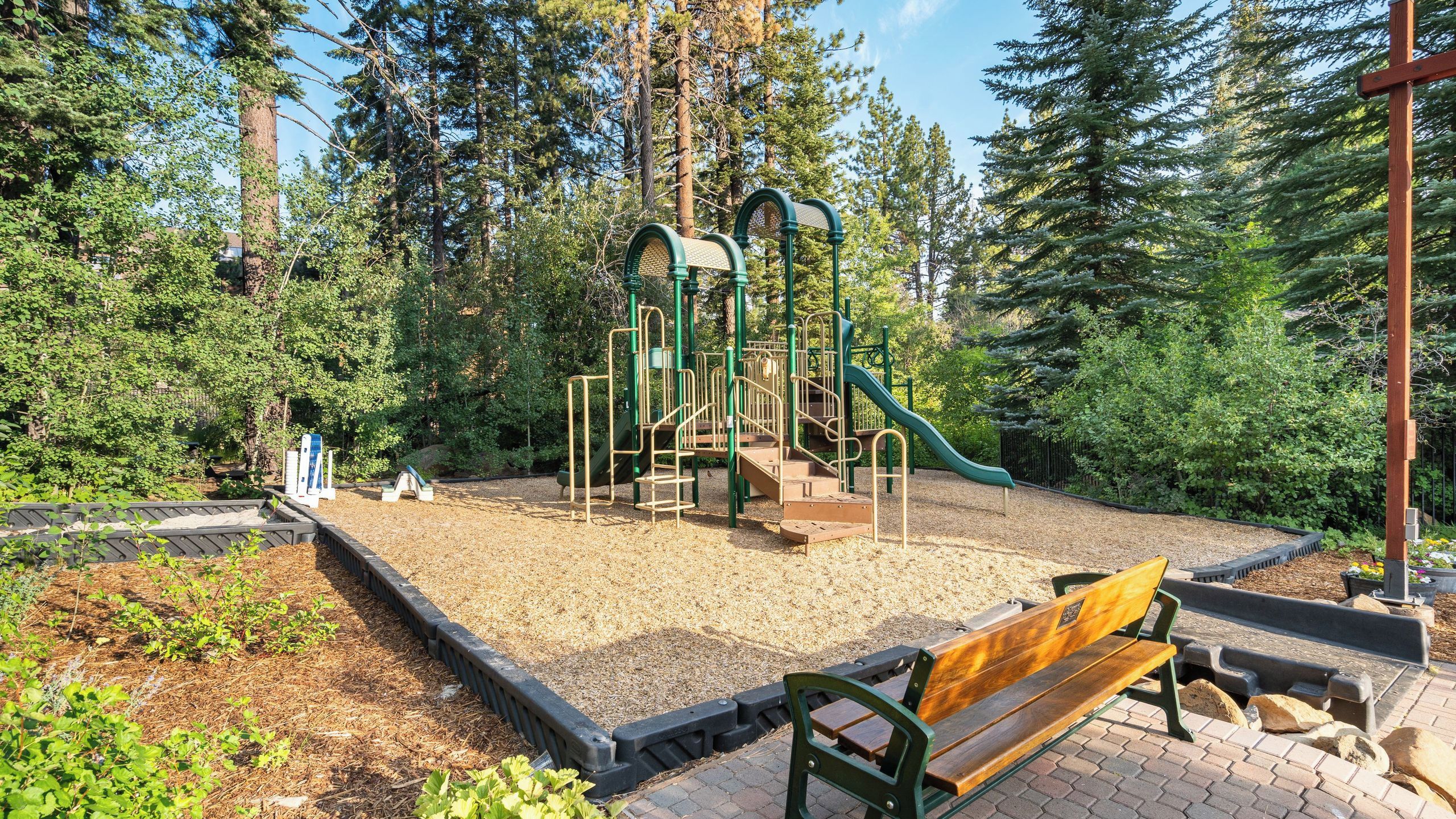 A playground with a slide and climbing structures, surrounded by trees.